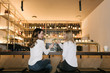 © Alvaro Hernandez/ADDICTIVE STOCK - Back view of two female friends smiling and clinking glasses of alcohol cocktails while spending time in bar of cozy restaurant
