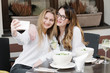© Alvaro Hernandez/ADDICTIVE STOCK - Two stylish female friends smiling and posing for selfie while sitting at table in cozy restaurant