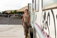 Strong Female Soldier Looking At Camera While Standing Near Grungy Military Vehicle In Countryside