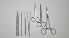 A Pair Of Stainless Steel Surgical Clamps, Scalpel Knife, Medical Grade Scissors, Forceps And Assorted Probes Displayed On A White Table.