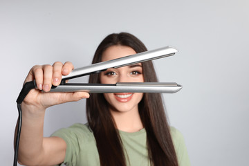 Wall Mural - Happy woman with hair iron on grey background