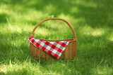 Fototapeta  - Wicker basket with blanket on green grass in park. Summer picnic