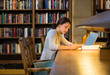 © ML Harris - Young woman female college university student with laptop computer studying in library on campus
