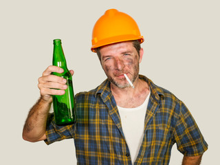 portrait of thirsty and tired constructor worker or builder man in safety helmet feeling exhausted holding cold beer bottle drinking and refreshing during work break