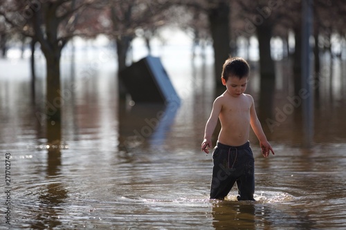 Fotomural Young toddler plays in water of flooded park after heavy rain storm