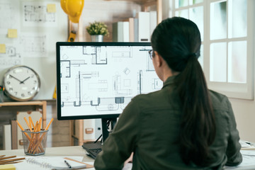 Back view portrait of asian woman engineer working on desktop computer with blueprints on screen in office. young female architect worker sitting in studio looking at pc screen interior design plan