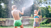 Two Childs, Brother And Sister, Have Fun, When Play With Watering Hose In Summer Garden