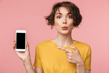 Shocked young beautiful woman posing isolated over pink wall background using mobile phone showing display.