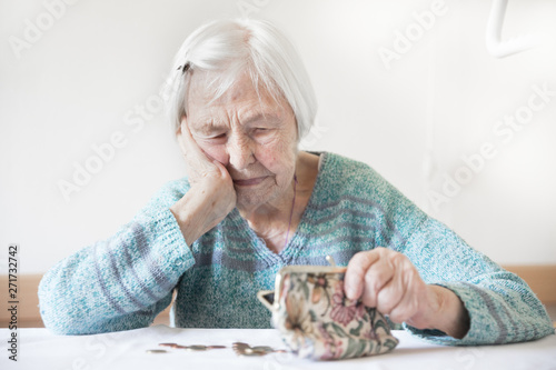 Fotomural Concerned elderly 96 years old woman sitting at table at home and counting remaining coins from pension in her wallet after paying bills