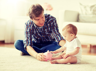 family, fatherhood, finances and parenthood concept - happy smiling young father and little baby playing with piggy bank at home