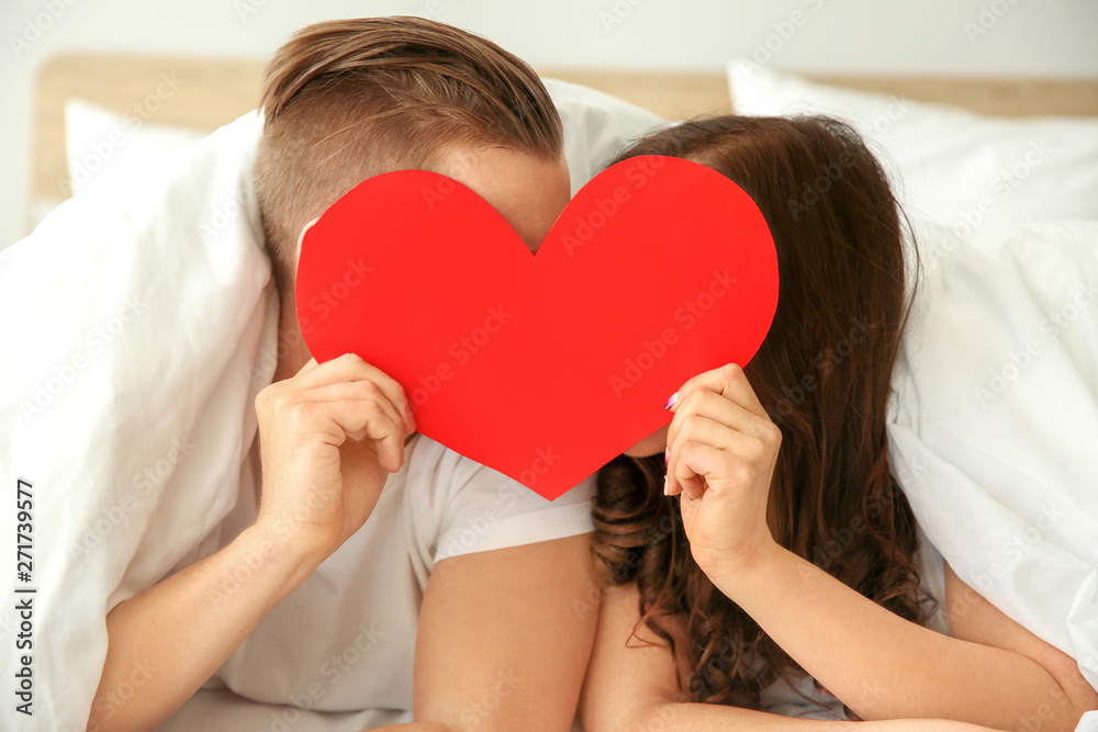 Happy young couple with paper heart lying in bed