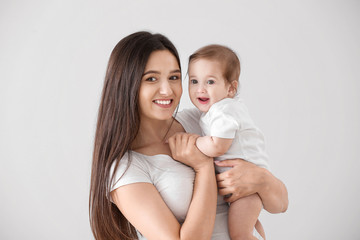 Wall Mural - Happy mother with cute little baby on light background