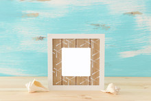 Blank White Photo Frame And Sea Shells Over Wooden Table And Pastel Blue Background. Ready For Photography Montage