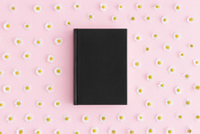 Top View Of A Black Book Mockup With Daisy Decoration On A Pink Background.