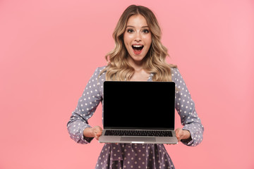 Amazing young woman posing isolated over pink wall background showing display of laptop computer.