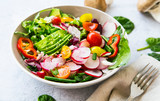 Fototapeta Storczyk - Fresh vegetable salad bowl closeup, healthy organic vegetables salad with radish, spinach, tomatoes, onion, avocado