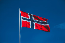 Norwegian Flag Against The Blue Sky. The Wind Blows Against The Blue Sky Without Clouds