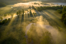 Sunny Misty Morning Nature Landscape Aerial View. View From Above Of Sun Rays Through Trees In Fog On Grassy Meadow Near River