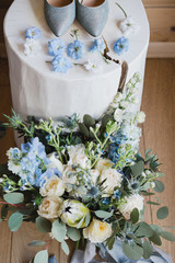 Botanic bridal chic. Bouquet with silk ribbons, female classic shoes, blue flowers composition on white wooden background.