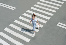 In The Summer On The Street At The Pedestrian Crossing Kid Girl In Fashion Clothes Cross The Road. From Top View. Shadow At Zebra Crossing