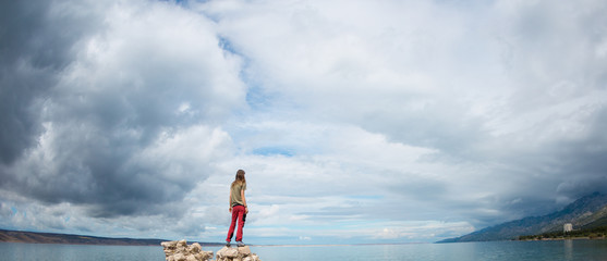 Wall Mural - The girl stands on a pile of stones and looks at the sea.