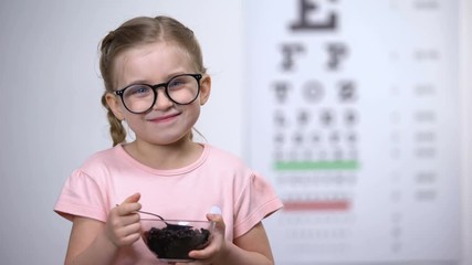 Wall Mural - Smiling girl in glasses eating blueberries, natural vitamins to improve vision