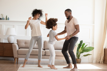 Wall Mural - Happy funny active african family with daughter dancing at home