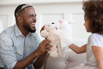 Funny african father wearing crown holding toy playing with daughter