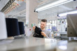 © Med Photo Studio - a young man analyzing a knitted piece of cloths near industrial knitted machines with black thread in cones
