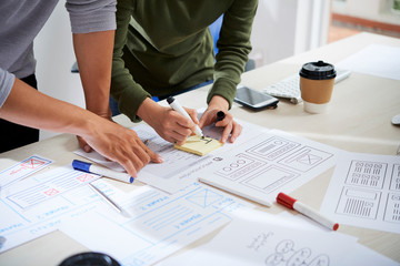 Hands of UX designers discussing documents and working on website wireframe design