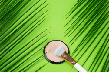 on a green background, there are two palm leaves on the edges, in the middle there is powder to improve the complexion and a brush