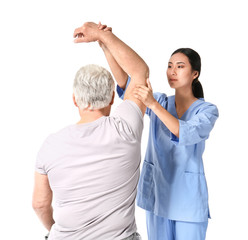 Poster - Young Asian physiotherapist working with mature man on white background