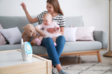 Modern baby monitor on table in room with woman and little child