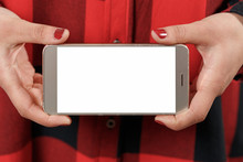 Smartphone With Blank White Screen Horizontally In Female Hands. Against The Background Of Red Plaid Shirt Girl