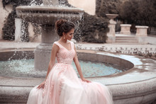 Beautiful Bride In Pink Wedding Dress. Outdoor Romantic Portrait Of Attractive Brunette Woman With Hairstyle In Prom Dress With Tulle Skirt Posing By Fountain At Park.