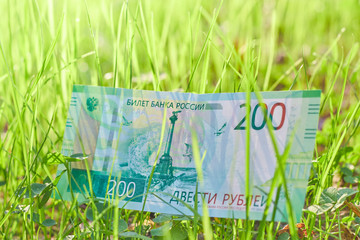 New Russian banknote Two hundred rubles in green grass in clear weather. Cash paper Russian green money.