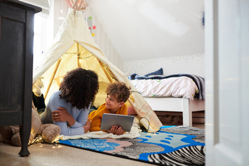 Wall Mural - Single Mother Playing With Son On Digital Tablet In Den In Bedroom At Home