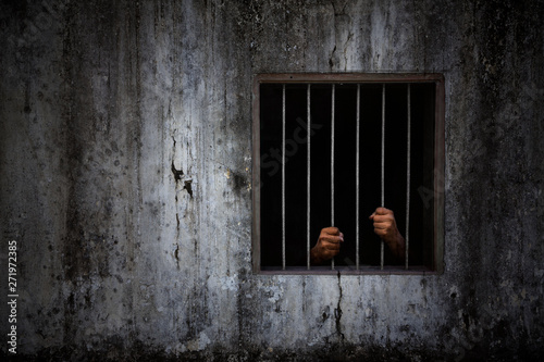 Fotografía Hands of the prisoner on rusty bar of window and old grungy prison cell wall
