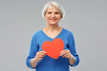 Poster - valentine's day, summer and old people concept - portrait of smiling senior woman with red heart over grey background