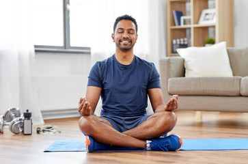 Wall Mural - fitness, meditation and healthy lifestyle concept - indian man meditating in lotus pose on exercise mat at home