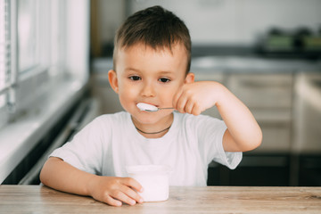 Wall Mural - Adorable little boy eating yogurt in the kitchen in the afternoon