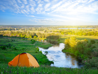 Wall Mural - orange tourist tent in green grass of hill above river