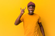 © Asier - Young black man wearing rastas over yellow background showing a horns gesture as a revolution concept.