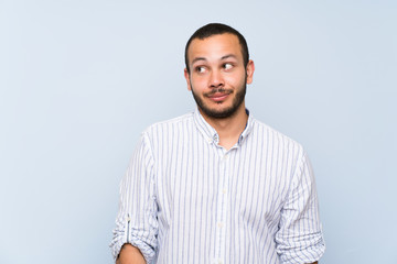 Colombian man over isolated blue wall making doubts gesture looking side