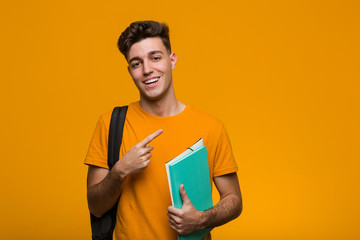 young student man holding books pointing with finger at you as if inviting come closer.
