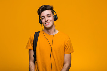 Wall Mural - Young cool student man listening to music with headphones smiling and raising thumb up