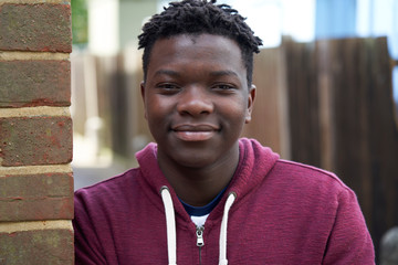 Portrait Of Smiling Teenage Boy Leaning Against Wall In Urban Setting