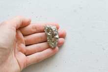 Stone Pyrite Lies In The Hand. Beautiful Iron In The Hand Of Natural Pyrite. On A White Background. Golden And Golden Stone Or Pyrite. Natural Stones. Minimalism