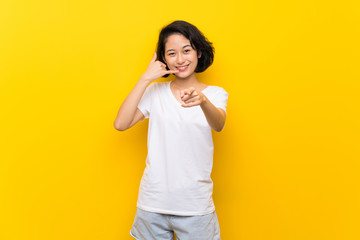 Asian young woman over isolated yellow wall making phone gesture and pointing front