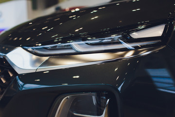 Close up of headlight detail of modern luxury car with projector lens for low and high beam. Front view of sport crossover vehicle head lamp. Concept of car detailing and light technology background.